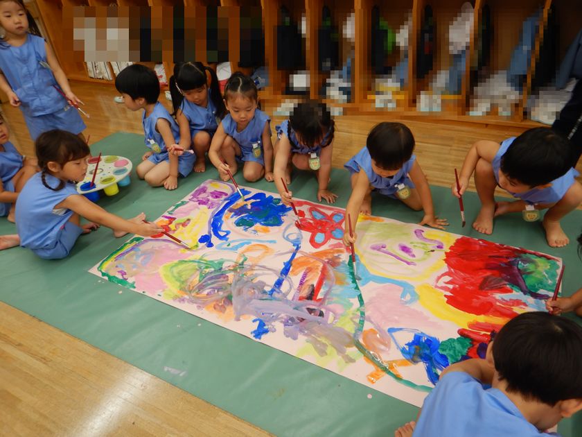 大きな画用紙に絵の具を使って絵を描く園児