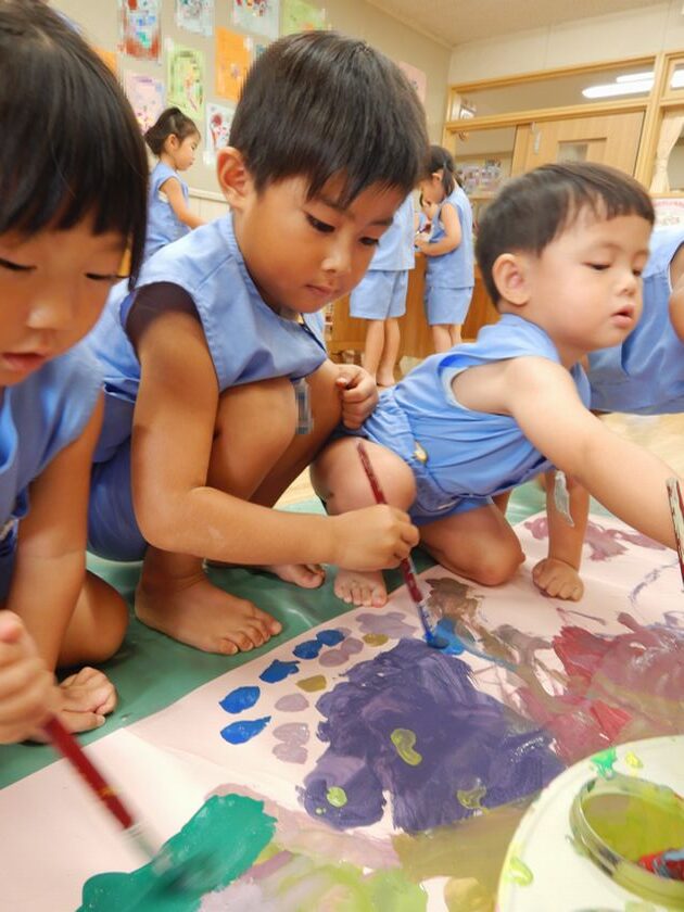 大きな画用紙に絵の具を使って絵を描く園児